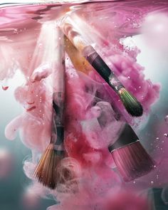 two brushes are floating in the water with pink paint on it and bubbles around them