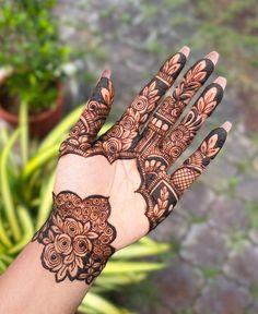 a person's hand with henna on it and some plants in the background