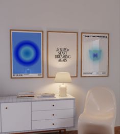 a white chair sitting next to a table with a lamp on it in front of two posters