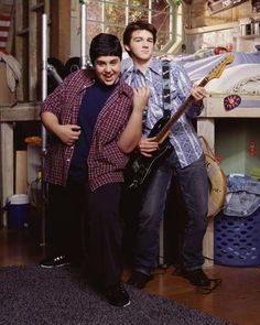 two young men standing next to each other in a room with bunk beds and guitars