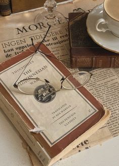 an old book with glasses on top of it next to a cup and saucer