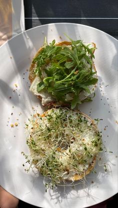 a white plate topped with a sandwich covered in veggies and sprouts