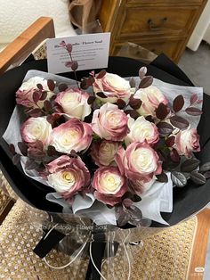 a bouquet of pink and white roses in a black vase on a table with a note