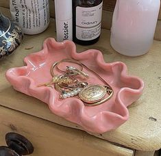 there is a pink tray that has some jewelry on it and other bottles next to it