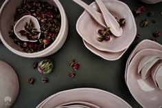 pink dishes with spoons and rose petals in them are arranged on a gray surface