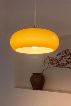 a yellow light hanging from the ceiling above a vase with flowers in it and a plant