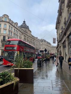 two red double decker buses driving down a street next to tall buildings