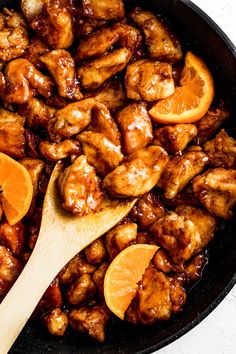 chicken and oranges cooking in a skillet with a wooden spoon on the side