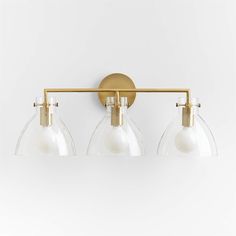 three light brass bathroom fixture with clear glass shades and gold metal fittings on an off - white wall