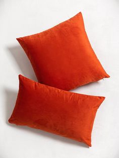 two orange pillows sitting next to each other on top of a white surface with one red pillow