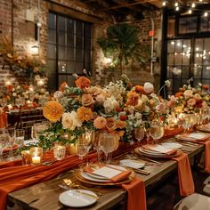 a long table is set with orange and white flowers in vases, candles, and napkins