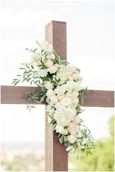 a cross decorated with white flowers and greenery