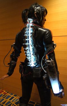 a woman dressed in black is holding a light up device while standing next to a wall