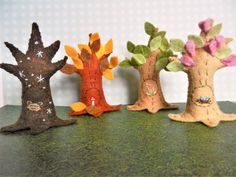 four small trees with leaves and flowers on top of a green tablecloth covered surface