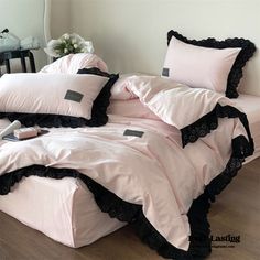 a bed with pink sheets and black ruffles on the bottom, along with pillows