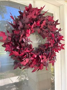 a wreath with red leaves hanging on the front door, in front of a window