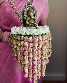 a woman in a pink saree holding a small statue made out of flowers and leaves