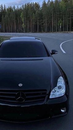 a black car parked on the side of a road in front of a wooded area