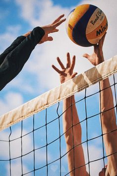 three people reaching up to hit a volleyball over the net