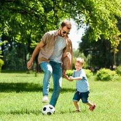 a father and son playing soccer in the park