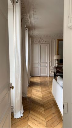 an open door leading to a bedroom with white walls and wood flooring on either side