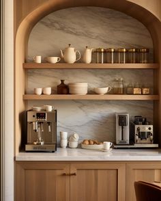 a coffee maker and some cups on a shelf in a room with wooden cabinets, marble counter tops and shelves