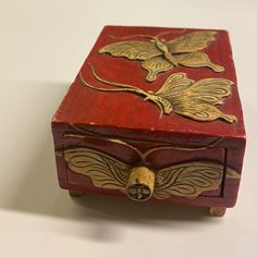 a red box with gold designs on the lid sitting on top of a white table