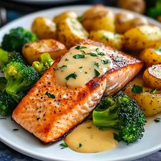 a white plate topped with salmon and broccoli covered in gravy next to potatoes