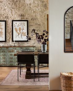 a dining room table and chairs in front of a stone wall with pictures on it