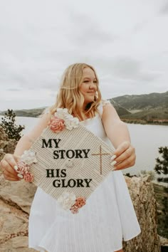 a woman holding up a sign that says my story his glory on the side of a mountain