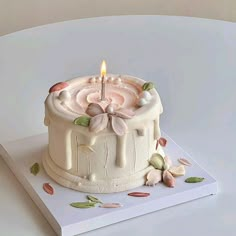 a white cake sitting on top of a table with a lit candle in the middle