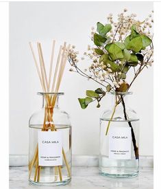 two vases with flowers and reed sticks in them on a marble countertop next to each other