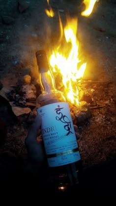 a bottle of booze sitting in front of a campfire with flames on the ground