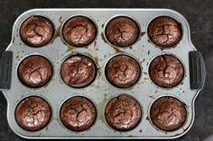 twelve chocolate cupcakes in a muffin tin on a counter top, ready to be eaten