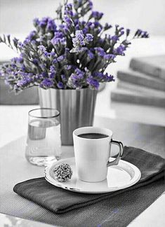 a cup of coffee sitting on top of a plate next to a vase filled with flowers