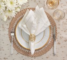 a place setting with napkins, silverware and white flowers on a table cloth