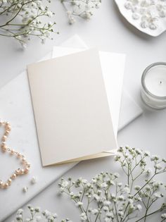 two blank cards sitting on top of a table next to some flowers and pearls around them