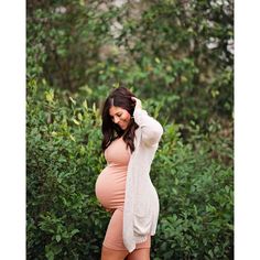 a pregnant woman is posing in front of some bushes