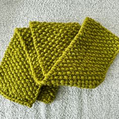 two pieces of green knitted cloth sitting on top of a white blanket covered floor