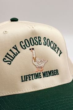 Introducing the Silly Goose Society Trucker Hat, a playful addition to your casual wardrobe. This hat features a beige body with charming dark green embroidery that reads "Silly Goose Society Lifetime Member" alongside an adorable goose illustration. The dark green bill adds a contrasting touch, while the adjustable back ensures a perfect fit for all. The back of the hat is embroidered with "The Happiest :)" to complete the fun and whimsical design. Perfect for adding a bit of humor and personal Cheap Whimsical Green Hats, Bachelorette Party Trucker Hats, Wedding Trucker Hats, Trucker Hat Designs Ideas, Fish Fear Me Hat, Dark Green Embroidery, Trucker Hat Designs, Goose Illustration, Hat Trends