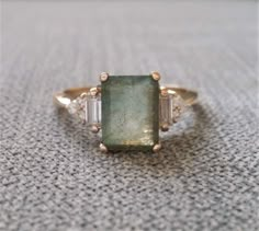 a close up of a ring with a green stone and two white stones on it