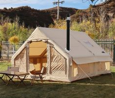 a tent set up in the grass with a table and chairs next to it,