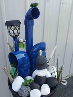 a blue water pump sitting on top of a black bowl filled with rocks and plants