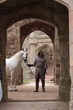 a woman standing next to a white horse in an archway with people walking by it