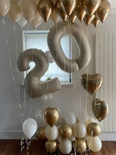 gold and white balloons are hanging from the ceiling in front of a number twenty sign