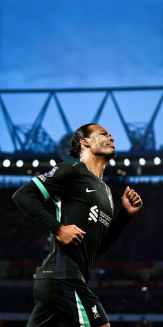 a man in black and green running on a soccer field with stadium lights behind him