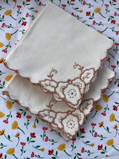 three pieces of cloth with embroidered flowers on them sitting on a tablecloth covered surface