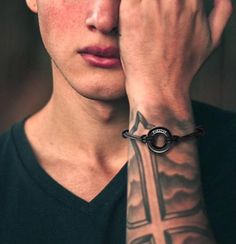 a young man with a cross tattoo on his arm holding his hand to his face