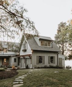 a white house sitting on top of a lush green field next to a lake and trees