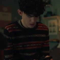 a young man looking at his cell phone in the living room while wearing a sweater